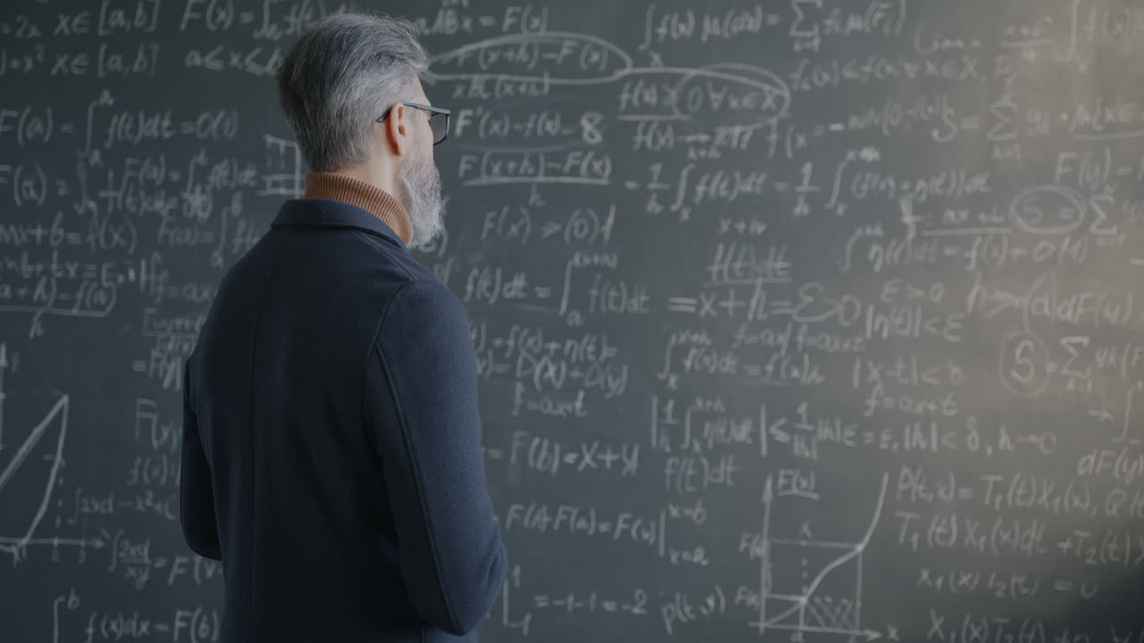 Professor facing away from camera in front of chalkboard with mathematical equations