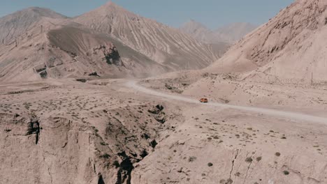 orange suv driving on a canyon road, next to a cliffside with mountain background