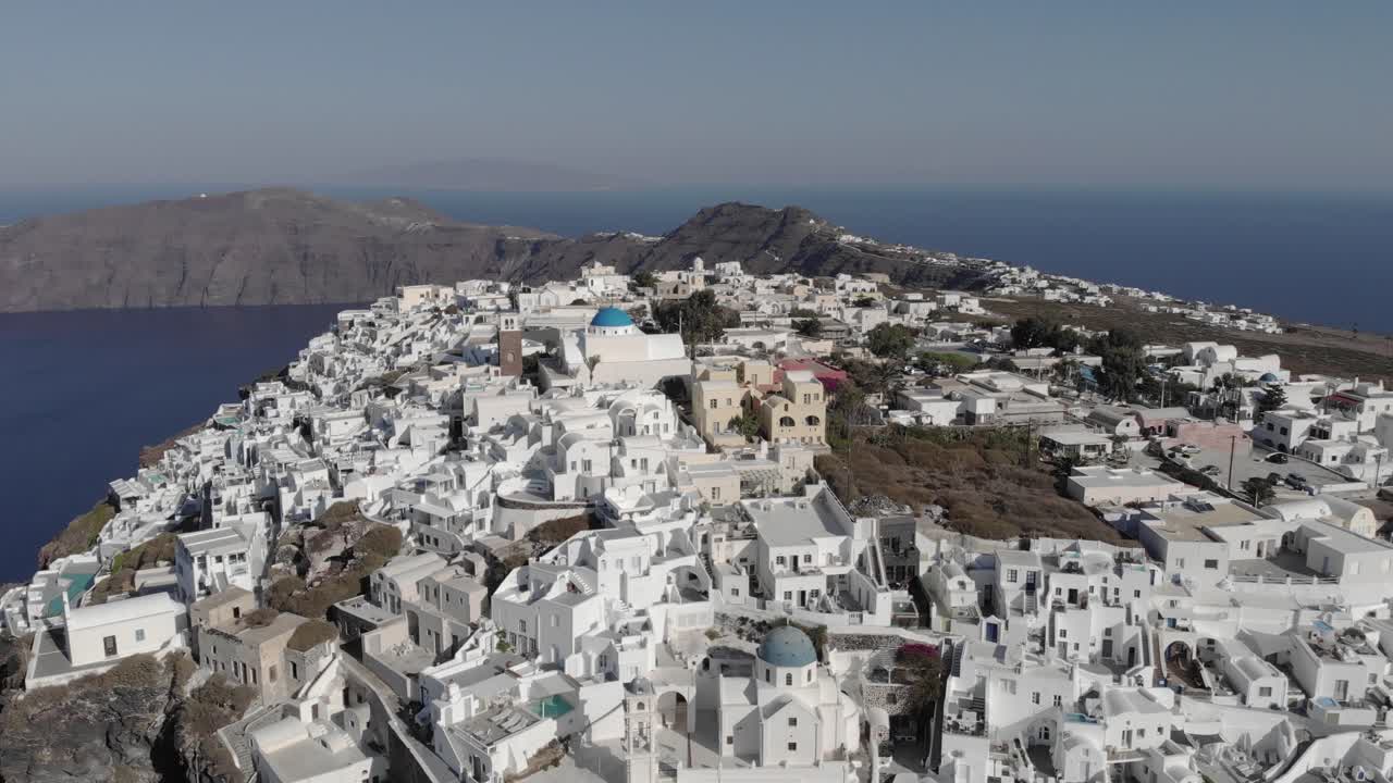 la antena en retirada revela casas blancas y brillantes en lo alto de un acantilado en santorini.