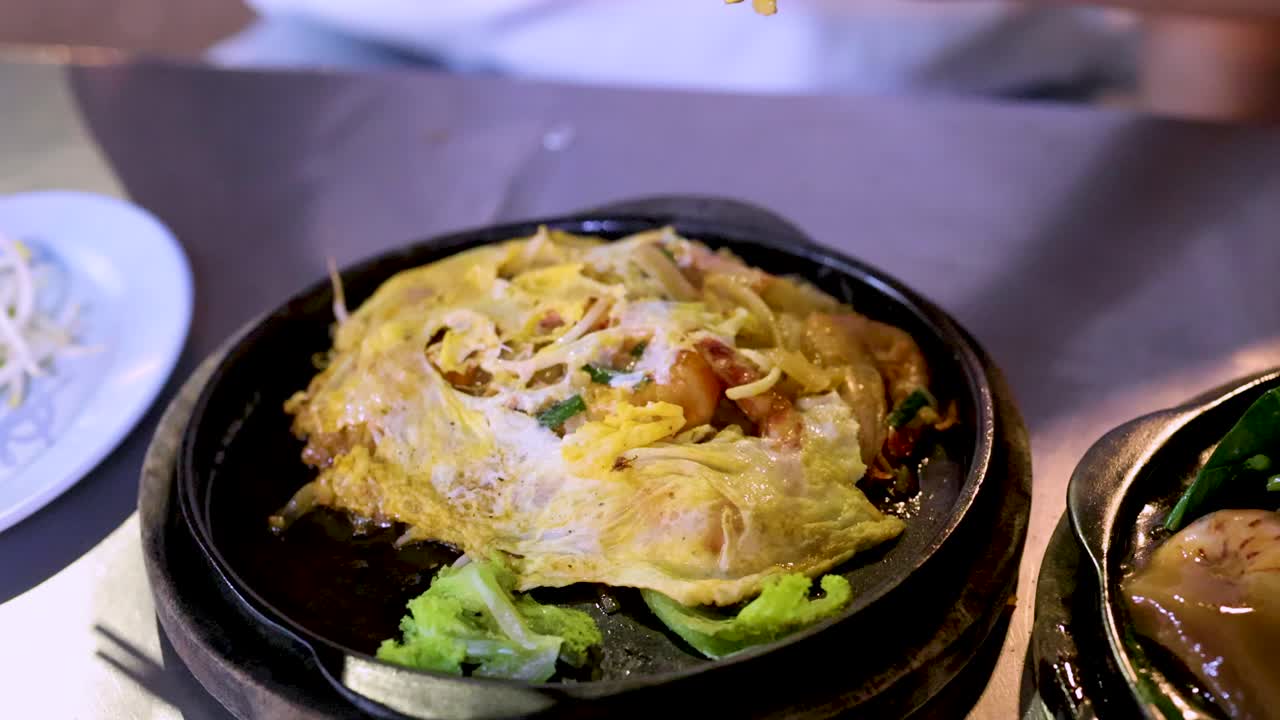 Pad Thai noodles with seafood on sizzling plate, vibrant lighting, close-up, slight camera movement