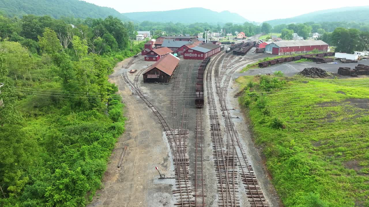 A visit to an old railway yard surrounded by green hills and rustic buildings. The area features tracks winding through the landscape, showcasing remnants of past train activity