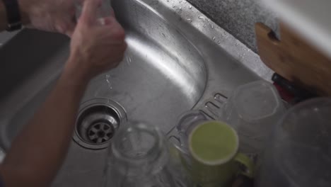 washing tall transparent glass and mug on a kitchen sink