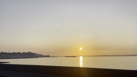 Wide-landscape-shot-of-the-sun-setting-over-a-costal-town-in-the-UK,-showing-a-calm-ocean-and-clear-skies