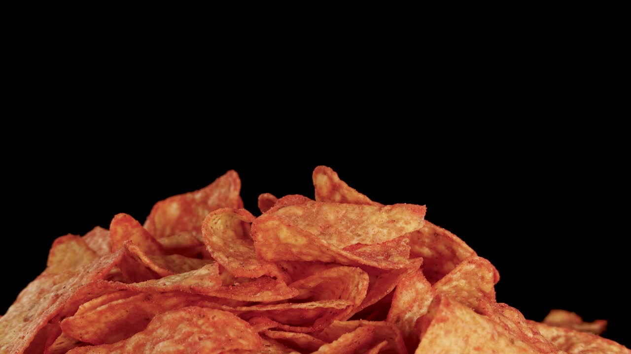 Crispy nacho tortilla chips fall onto a pile, shot in slow motion against black background