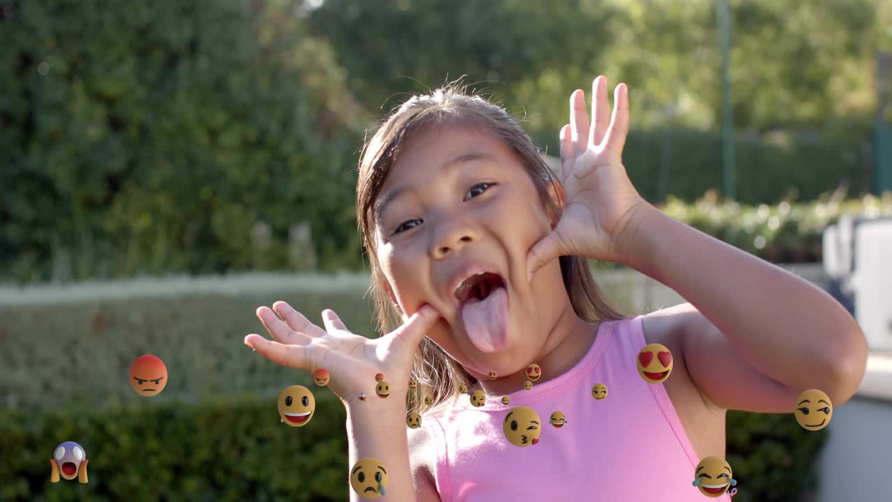 Depois de um sorriso, garota puxando as bochechas, mostrando a língua, emojis flutuando ao redor das mãos, rede social