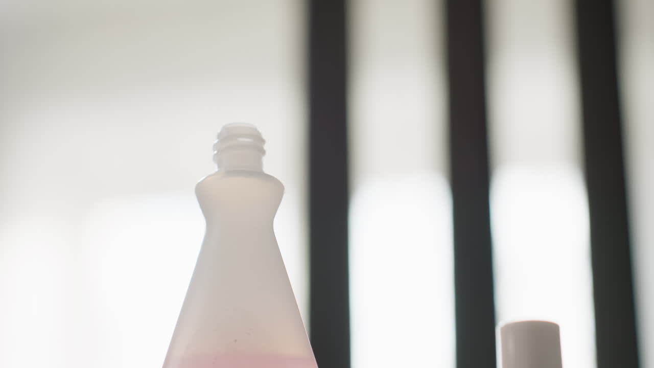 Close up lower view shows female hand removing cap from white nail polish remover bottle, gentle twist motion in home setting, pink lid highlighted, beauty care moment before manicure on table