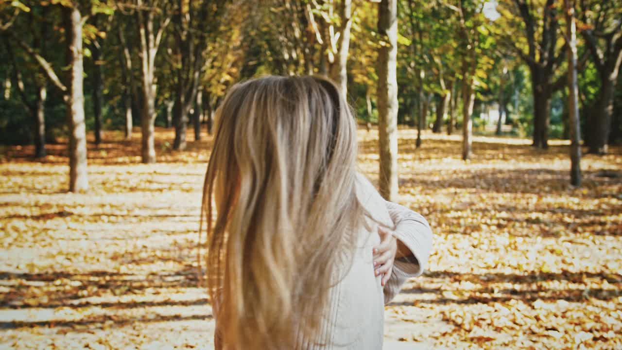 어린 엄마는 웃고, 작은 딸을 팔에 들고 가을 공원에서 산책하는 동안 그들의 축을 중심으로 그녀와 함께 순환하고 있습니다.