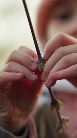 primer plano de las manos de una niña tocando delicadamente una rama seca del árbol, capturando un momento de exploración y curiosidad. la niña, vestida con una chaqueta rosa y gorra