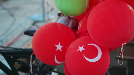 colorful punch balloons for kids and red balloons with turkish flag are attached to a bike for sale in the street