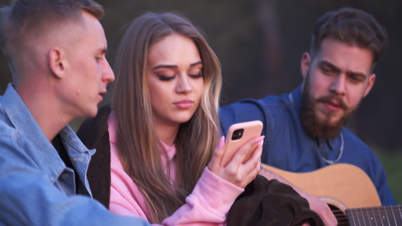Young people playing music, singing and having fun on picnic. Couple in the center looking at each other, moving their heads to the rhythm of the music.
