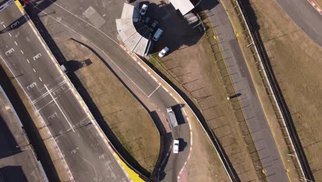 toma aérea de arriba hacia abajo de un camión remolcando un auto de carreras después de un accidente en la pista de carreras
