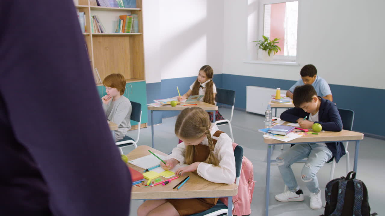 Multiethnic Group Of Kids In Classroom Writing In Their Notebook During English Class At School