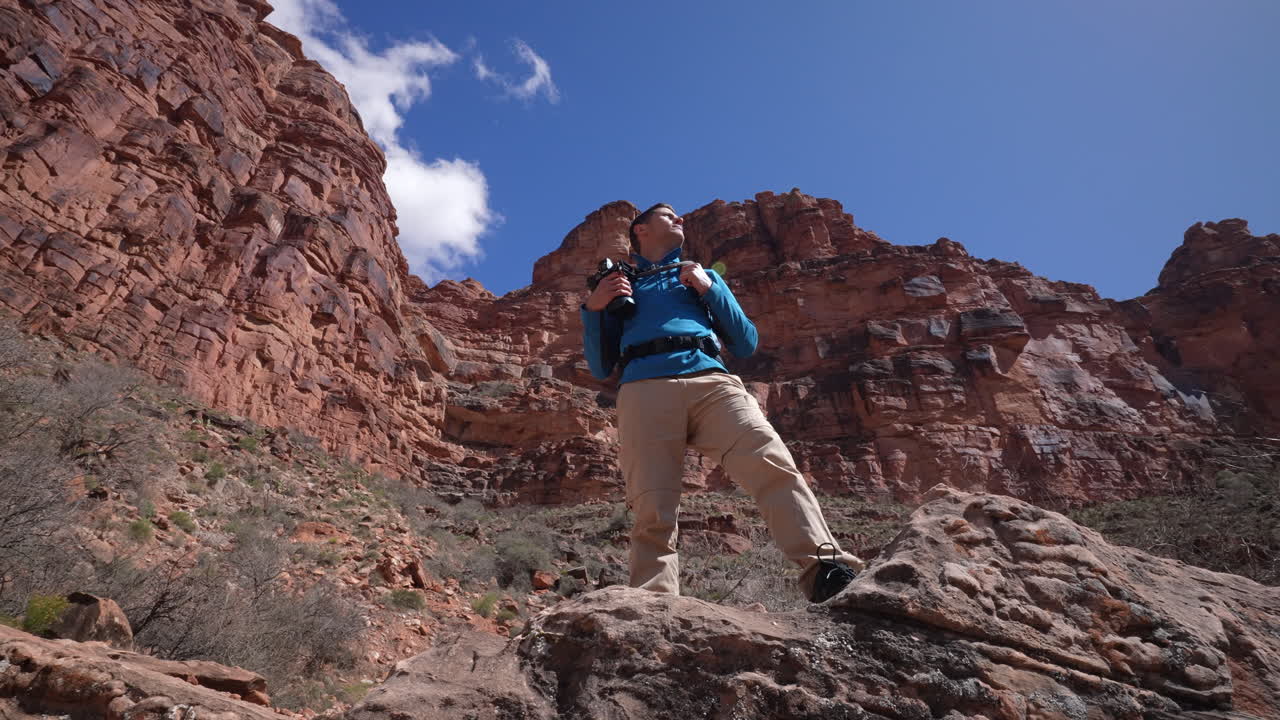 joven mirando con orgullo a las montañas del desierto en una caminata en la naturaleza sosteniendo su cámara - confiado, orgulloso, logrado, éxito