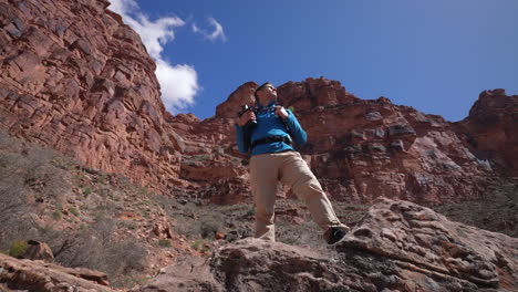 Young-man-proudly-looking-out-at-the-desert-mountains-on-a-hike-in-nature-holding-his-camera---confident,-proud,-accomplished,-success