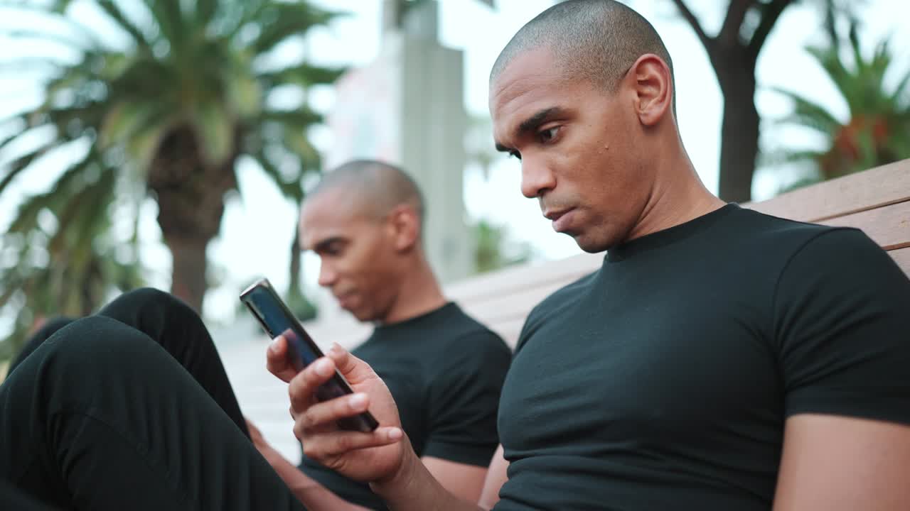 Two concentrated bald African brothers looking at phones