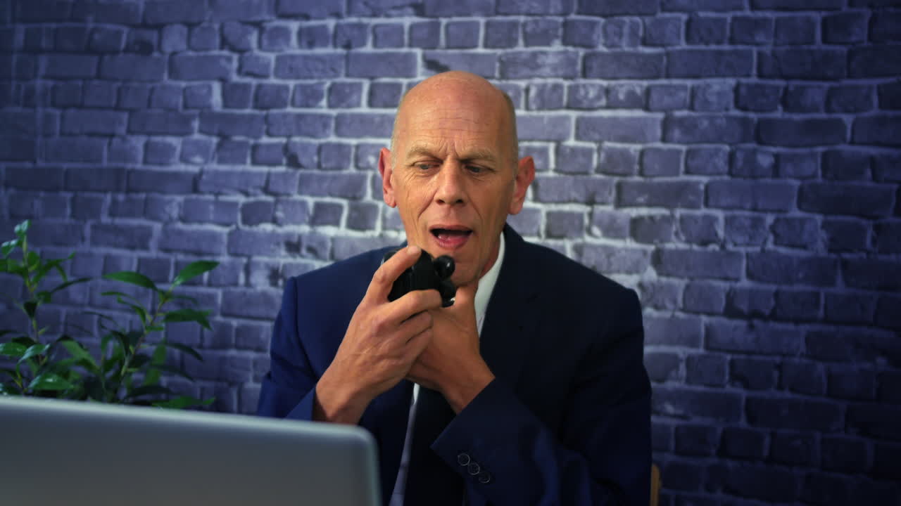 A business man shaving with an electric razor in the office at work in front of a laptop computer