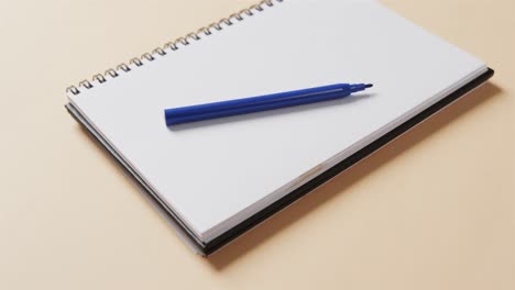 close up of blue marker on notebook with beige background, in slow motion