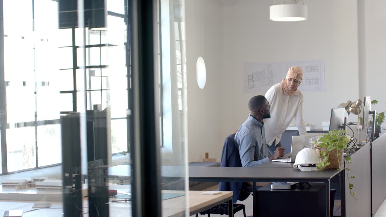 Discussing project, colleagues using laptop and documents in modern office setting