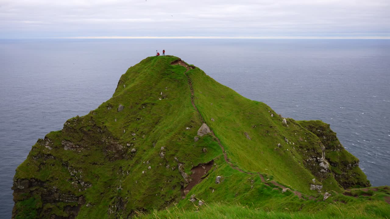 Two hikers on a cliff's edge next to the Atlantic Ocean taking pictures