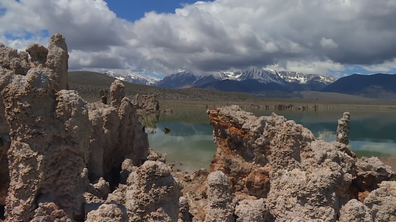 Torri di tufo frastagliate in primo piano, Lago Mono riflettente a metà campo, Twin Peaks innevate in lontananza, movimento di inclinazione verso l'alto.