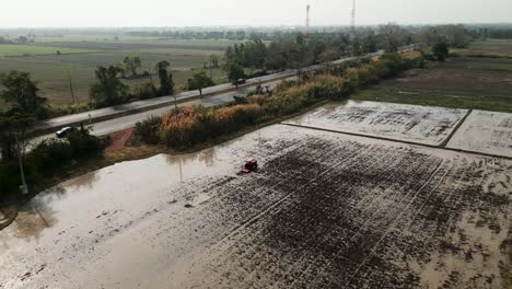 aerial view of a tractor cultivating a flooded rice field next to a rural road