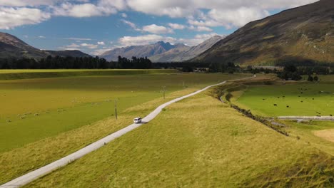 van driving through scenic mountains and green pasture landscape of earnslaw burn track in otago, new zealand - aerial shot
