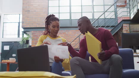 Happy-african-american-female-and-male-business-colleagues-reading-files-at-office