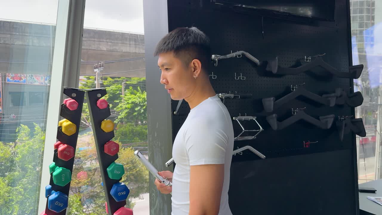 Young man selects cable machine attachment in bright, modern gym with large windows