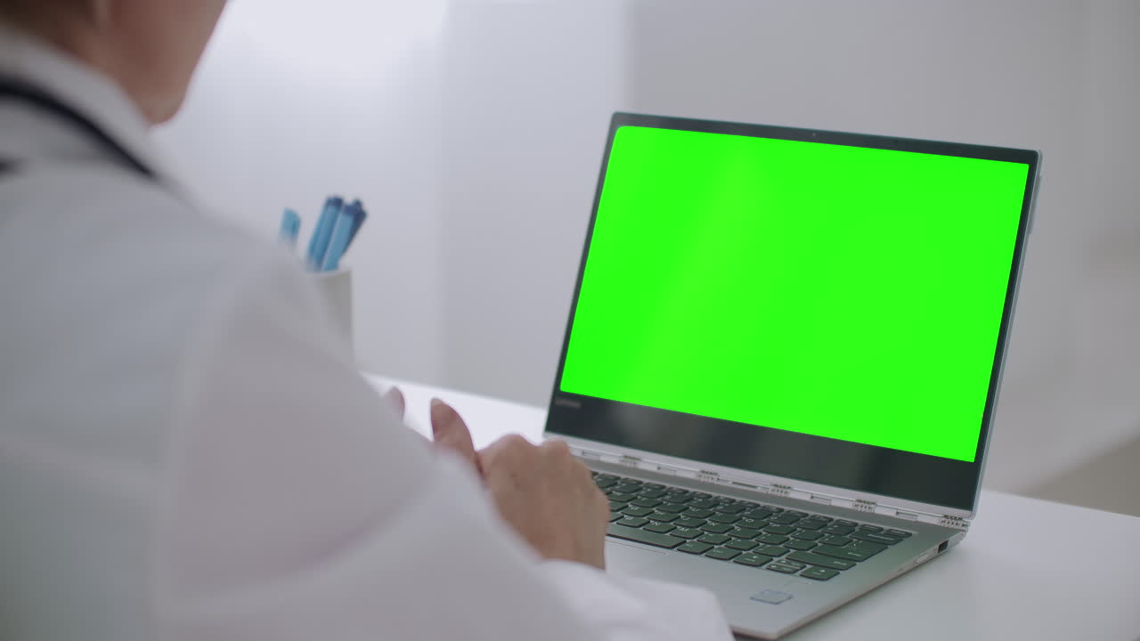 la médica está consultando en línea mirando la pantalla verde de la computadora portátil para la tecnología de llave cromática escuchando y respondiendo gesticulando con las manos