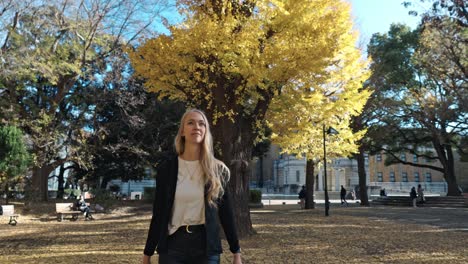 a serene autumn scene in tokyo, where a woman strolls through a park filled with vibrant yellow foliage.