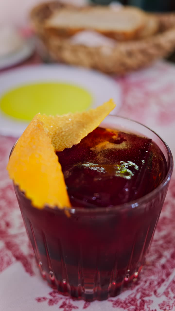 Close up of a negroni cocktail on a red and white tablecloth at a restaurant. Vertical
