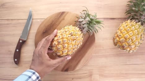 mano sosteniendo una piña en una tabla de cortar