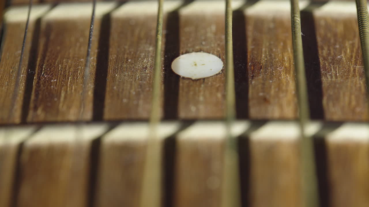 Scatto macro in primissimo piano di corde di chitarra acustica con un movimento di messa a fuoco selettiva lungo la tastiera in legno. Ideale per documentari musicali e montaggi artistici.