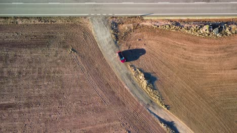 red car standingon a dirt road through golden fields in lleida, catalonia, aerial view