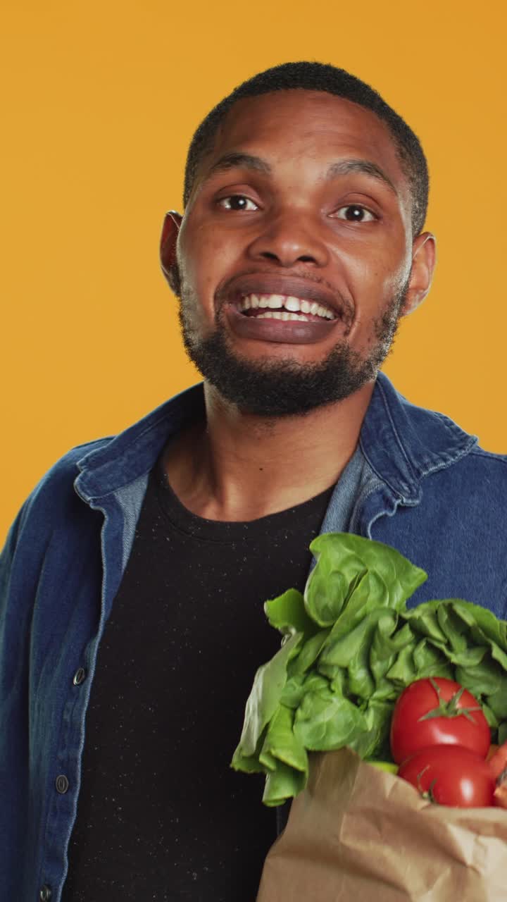 Giovane uomo di colore espressivo che tiene una busta della spesa con verdure fresche