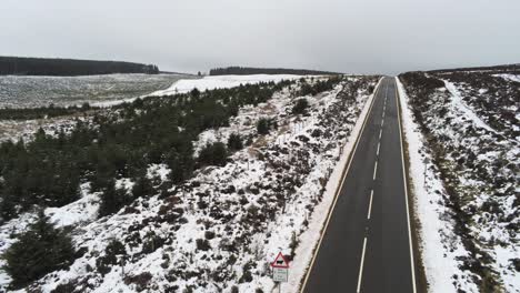 Antenne,-Die-Einer-Langen,-Leeren-Straße-In-Die-Ferne-über-Verschneite-Landschaftsmoore-Im-Hochland-Folgt