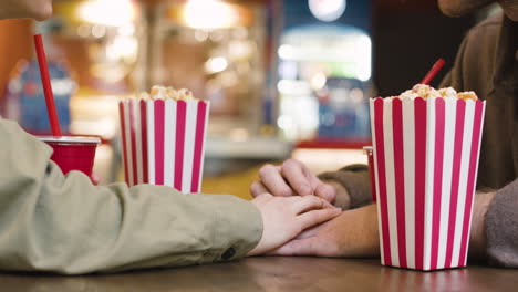 loving couple holding hands while sitting at table in the cinema snack bar 1