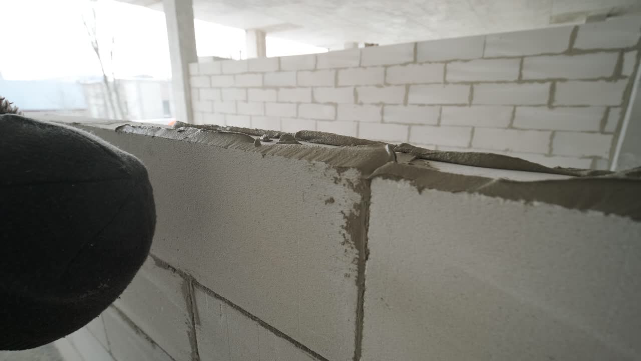 Il maestro esegue la posa di un muro di blocchi in calcestruzzo aerato con attrezzi e malta adesiva.