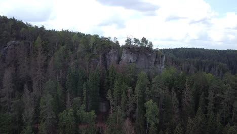 drone flies over treetops and rock formations in the saxony wilderness reserve park with blue sky and clouds