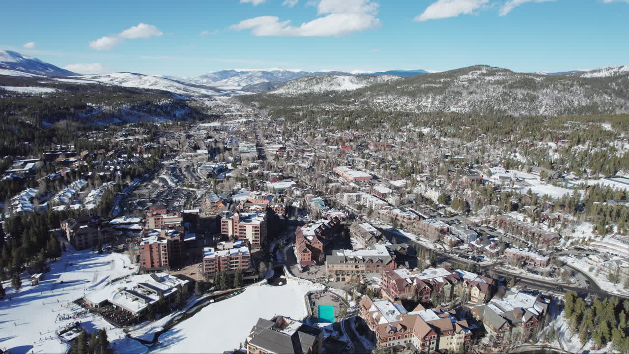 A wide aerial of peaceful and beautiful snow-covered Breckenridge, as cars carrying skis and snowboards drive into the popular Colorado mountain town for a ski vacation at the world famous resort.