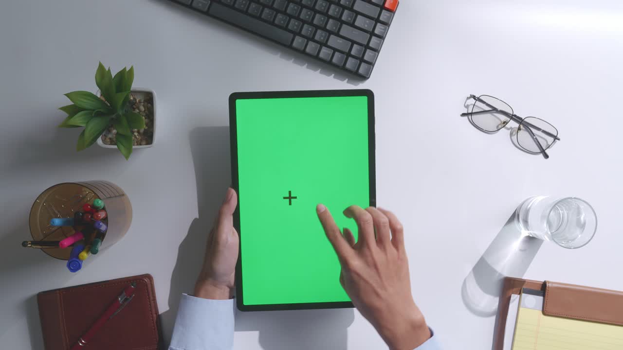 верхний вид ноутбука с макетным зеленым экраном chromakey на деревянном офисном столе рядом с ноутбуком с ручками, очками и стаканом воды.