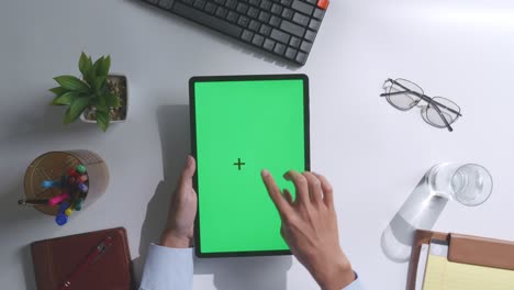 vista de arriba hacia abajo de una computadora portátil con pantalla verde simulada pantalla chromakey en un escritorio de oficina de madera al lado de la libreta con bolígrafos, gafas y un vaso de agua.