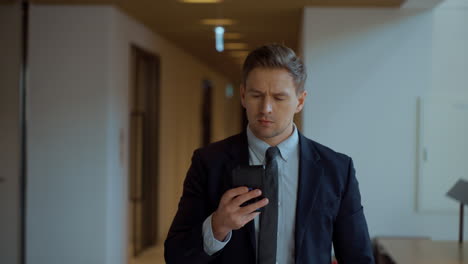 anxious troubled businessman looking at smartphone while walking along office corridor - slow motion tracking front view