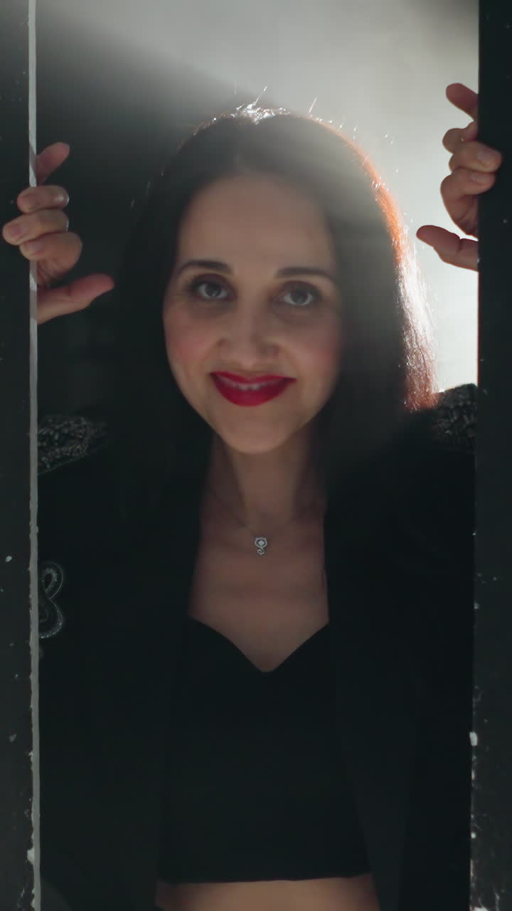 Serene woman in black outfit framed by a doorway, bathed in soft light with a slow camera zoom as she smiles gently