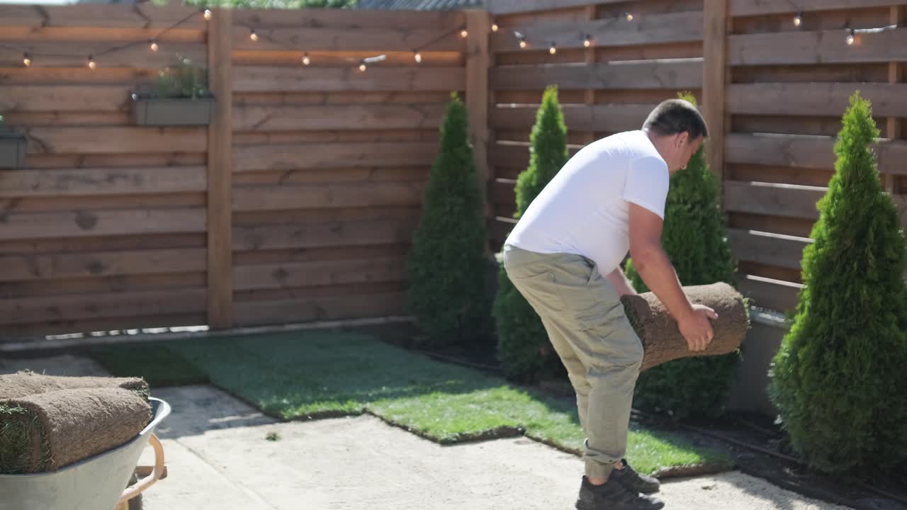 Man Laying Sod Grass in Backyard Garden for Lawn Installation and Landscaping Project, Focused on Home Improvement and Outdoor Maintenance for a Fresh, Green Lawn in a Residential Yard