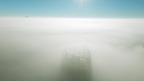 drone tilts up, unveiling lone skyscraper piercing through thick clouds at sunrise—a cinematic marvel in the empty cityscape