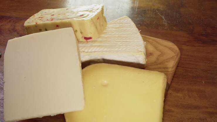Four types of hard cheese are stacked on wooden chopping block, food