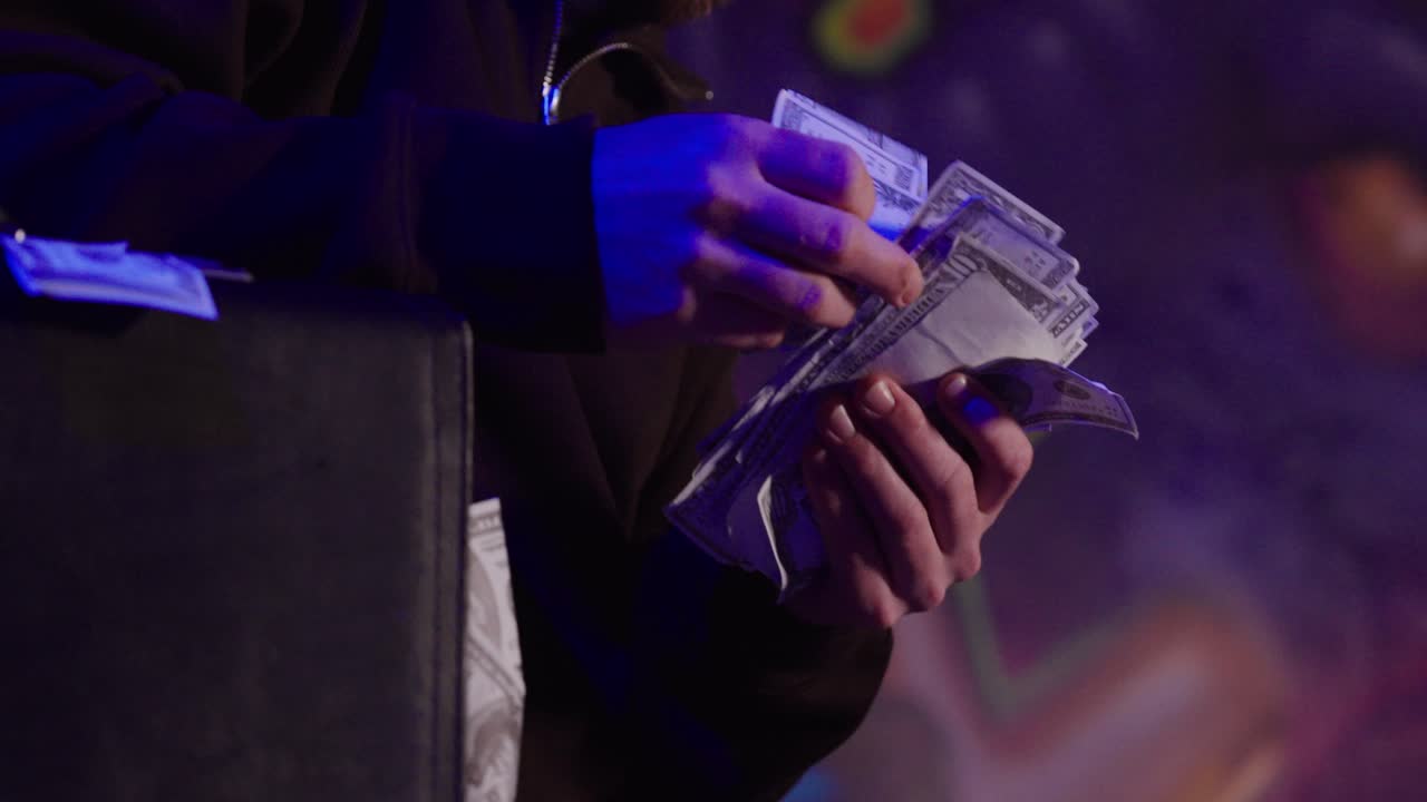 Close-up of hands counting cash taken as bribe under dramatic blue lighting. Concept of corruption, illegal payments, financial crime, secrecy, and unethical behavior