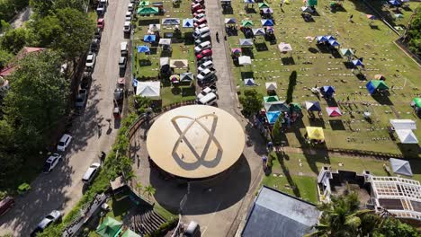 aerial drone footage of memorial park in surigao city - philippines, on all souls day, showing cars parked and gazebos on a field surrounded by lush greenery