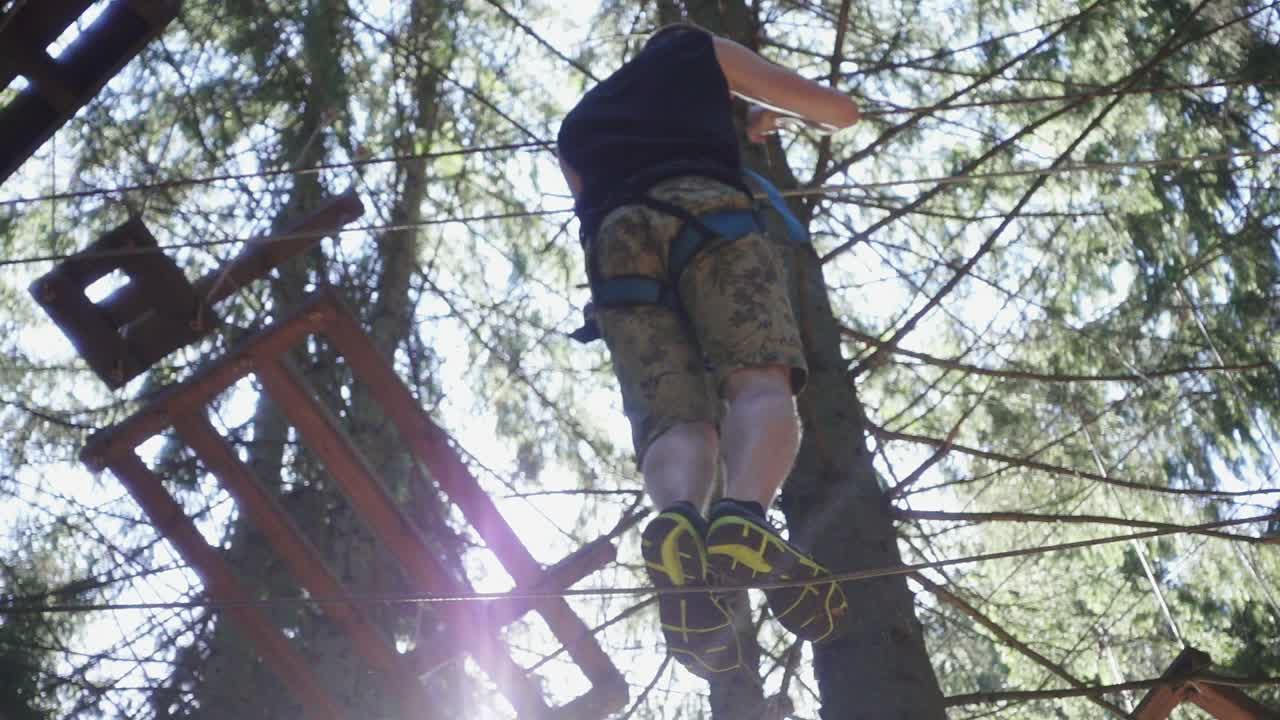 Young man in safety equipment walking on rope on high in summer climbing park
